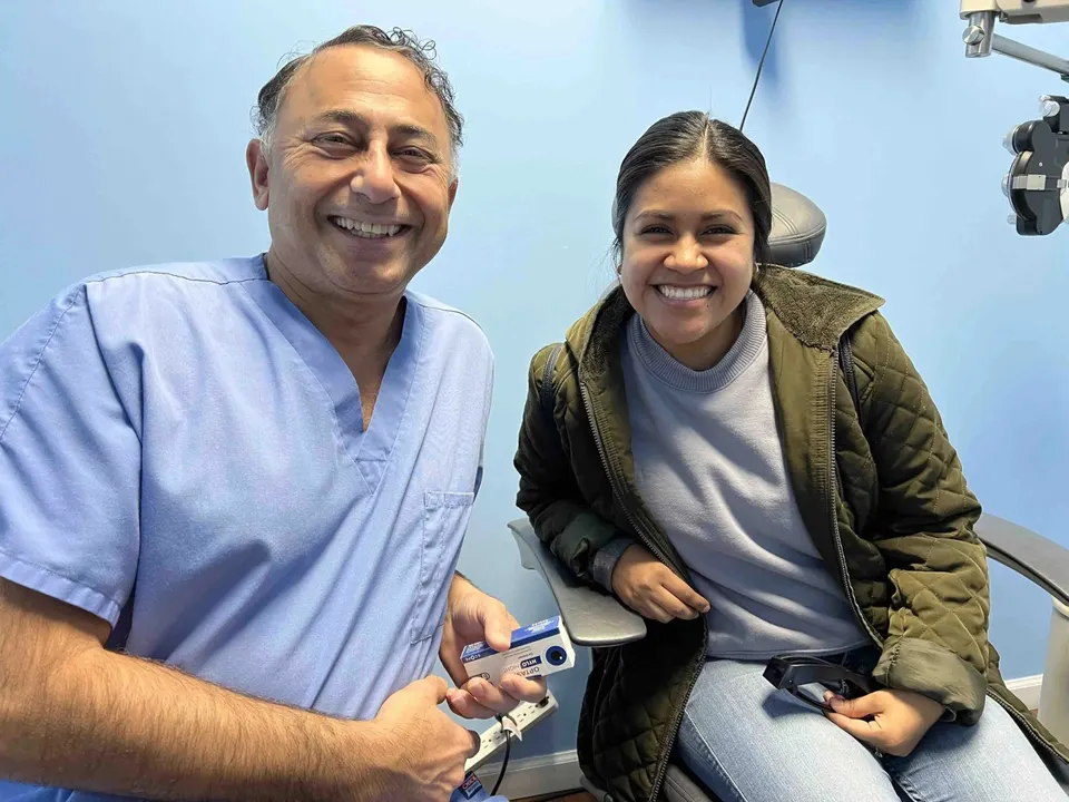 Dr. Khanna in blue scrubs smiling beside a patient seated in an exam chair