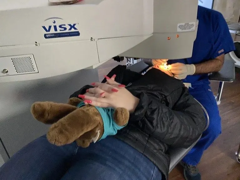 Patient lying under a VISX excimer laser during LASIK, holding a teddy bear