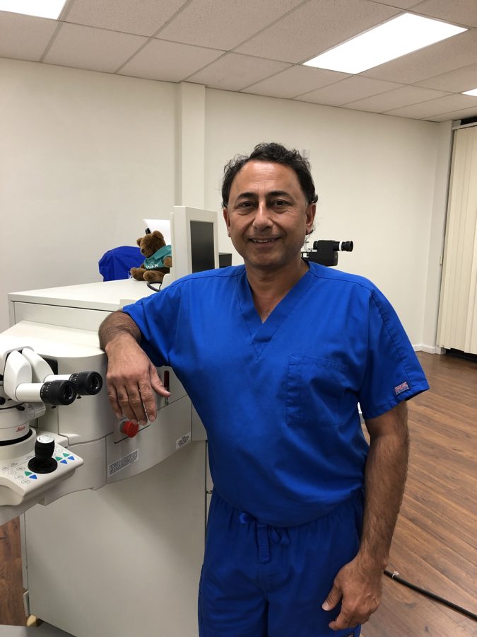 Dr. Rajesh Khanna in blue scrubs leaning on an excimer laser in a Khanna Vision Institute laser suite
